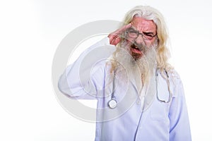 Studio shot of stressed senior bearded man doctor having headach