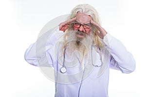 Studio shot of stressed senior bearded man doctor having headach