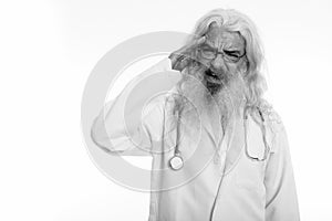 Studio shot of stressed senior bearded man doctor having headache