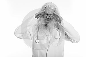 Studio shot of stressed senior bearded man doctor having headache with both hands on head