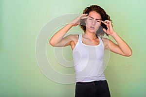 Studio shot of stressed teenage girl having headache against gre