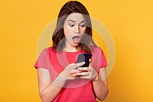 Studio shot of stupefied Caucasian brunette woman posing with widely open mouth, reads incredible news in Internet or shocking