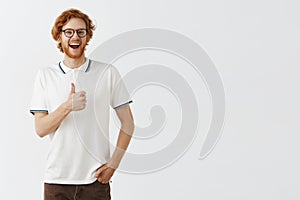 Studio shot of supportive entertained and amused happy redhead bearded guy in casual polo shirt and black glasses