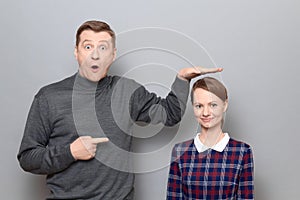 Tall man is showing height of short woman and pointing at her