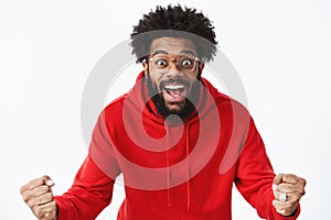 Studio shot of surprised and thrilled african american guy clenching fists in joy and amazement popping eyes and smiling