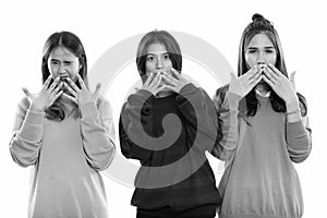 Studio shot of three young Asian woman friends covering mouth while looking shocked together