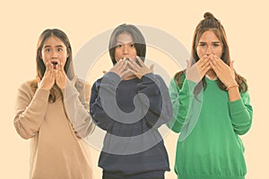 Studio shot of three young Asian woman friends covering mouth while looking shocked together