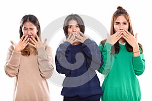 Studio shot of three young Asian woman friends covering mouth wh