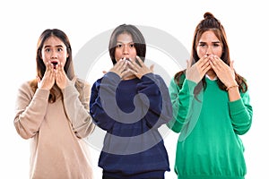 Studio shot of three young Asian woman friends covering mouth wh