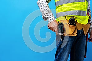 Studio shot of unknown handyman with hands on waist and tool belt with construction tools