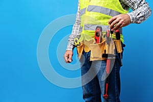 Studio shot of unknown handyman with hands on waist and tool belt with construction tools