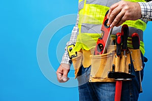 Studio shot of unknown handyman with hands on waist and tool belt with construction tools