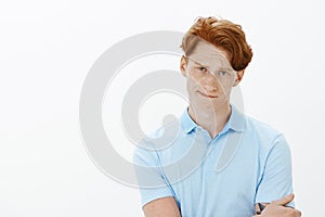 Studio shot of unsure good-looking redhead man with freckles, biting lip, frowning and gazing with doubt at camera
