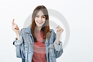 Studio shot of upbeat good-looking girl with brown hair, raising hands and smiling broadly after successful interview