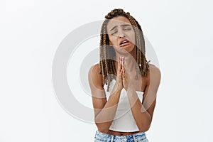 Studio shot of whining miserable and desperate cute young dark-skinned female with dreadlocks making sad face stooping