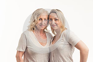 Studio shot on white background of two similarly looking middle-aged women, standing close to each other placing their