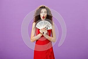 Studio shot of woman being lucky in casino winning lots of cash holding money in hands saying wow with folded lips