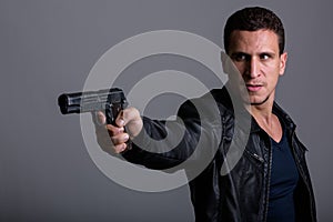 Studio shot of young angry muscular Persian man aiming to shoot