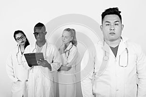 Studio shot of young Asian man doctor with diverse group of multi ethnic doctors thinking while looking at clipboard