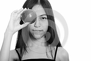 Studio shot of young Asian teenage girl covering eye with red apple