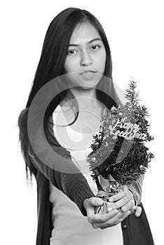 Studio shot of young Asian teenage girl giving Happy New Year tree with focus on the tree