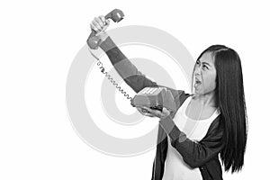 Studio shot of young Asian teenage girl holding old telephone looking angry