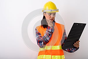 Studio shot of young Asian woman construction worker reading on