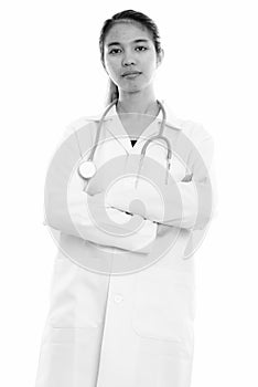 Studio shot of young Asian woman doctor standing with arms crossed