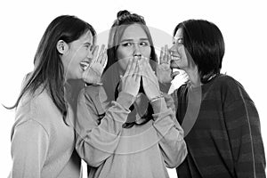 Studio shot of young Asian woman looking shocked with both friends whispering on each side