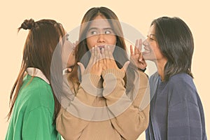 Studio shot of young Asian woman looking shocked with both friends whispering on each side