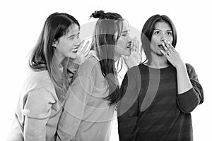 Studio shot of young Asian woman looking shocked with both friends whispering on one side