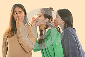 Studio shot of young Asian woman looking shocked with both friends whispering on one side