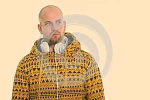 Studio shot of young bald muscular man wearing headphones around neck while thinking