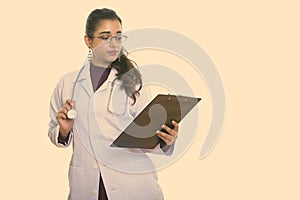 Studio shot of young beautiful Indian woman doctor reading on clipboard