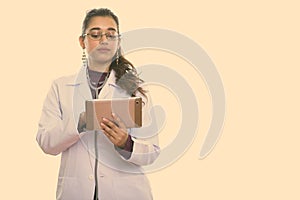 Studio shot of young beautiful Indian woman doctor using digital tablet