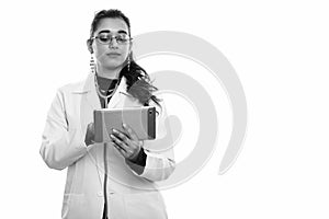 Studio shot of young beautiful Indian woman doctor using digital tablet