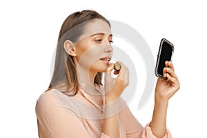 Studio shot of a young beautiful woman applying lip balm in front of a mirror.