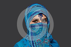 Studio shot of a young beautiful woman wearing the blue hijab decorated with sequins and jewelry. Arabic style.