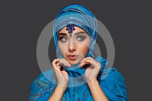 Studio shot of a young beautiful woman wearing the blue hijab decorated with sequins and jewelry. Arabic style.