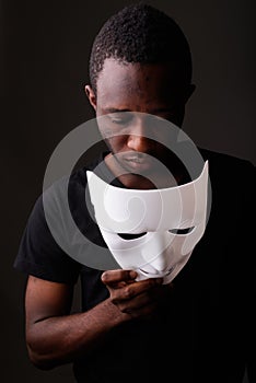 Studio shot of young black African man in dark room holding mask