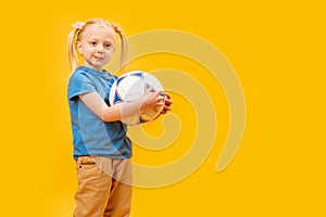 Studio shot of young blonde girl holding soccer ball against yellow background. Child and football. Copy space, mockup