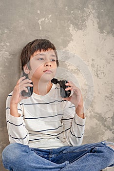 Studio shot of a young boy wearing a white shirt and jeans with headphones siting on the floor by the wall and thinks or sad about