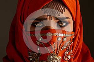 Studio shot of a young charming woman wearing the terracotta hijab decorated with sequins and jewelry. Arabic style.