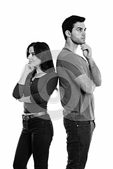 Studio shot of young couple standing while thinking and looking up together with back to back