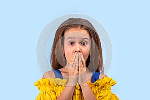 Studio shot of a young  girl  covering her mouth with her hands in fright against blue background