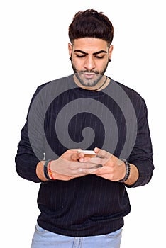 Studio shot of young handsome Indian man using mobile phone isol