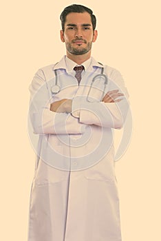 Studio shot of young handsome man doctor standing with arms crossed