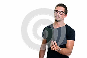 Studio shot of young handsome man holding book while thinking wi