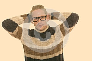 Studio shot of young handsome man thinking while wearing eyeglasses with hands behind head