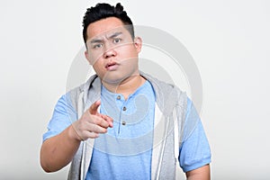 Portrait of stressed young overweight Asian man pointing at camera